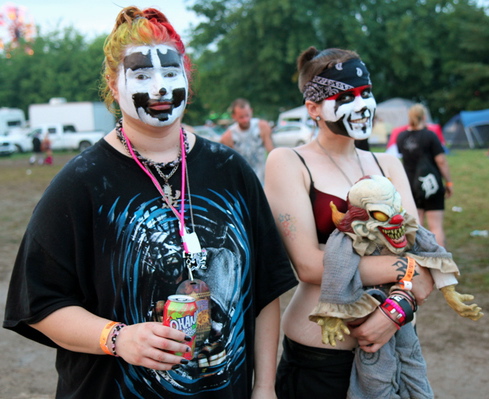 This is a picture of two female Jugalettes with their faces painted like clowns, one carrying a creepy clown doll.