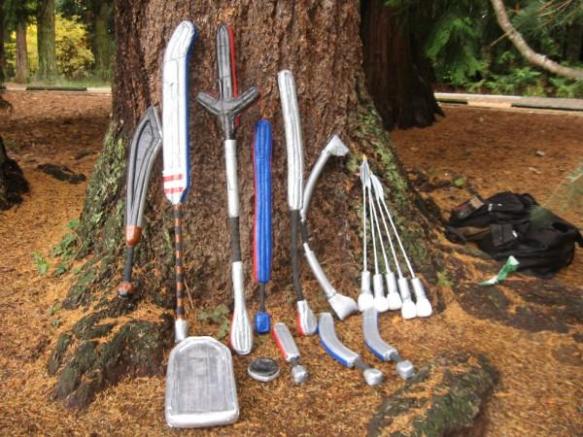 This is a photo of many different homemade LARP foam weapons leaning against a tree in the woods