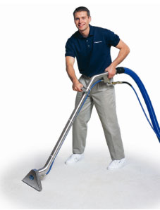 This is a picture of a young man in khakis and a polo shirt steam cleaning a carpet.